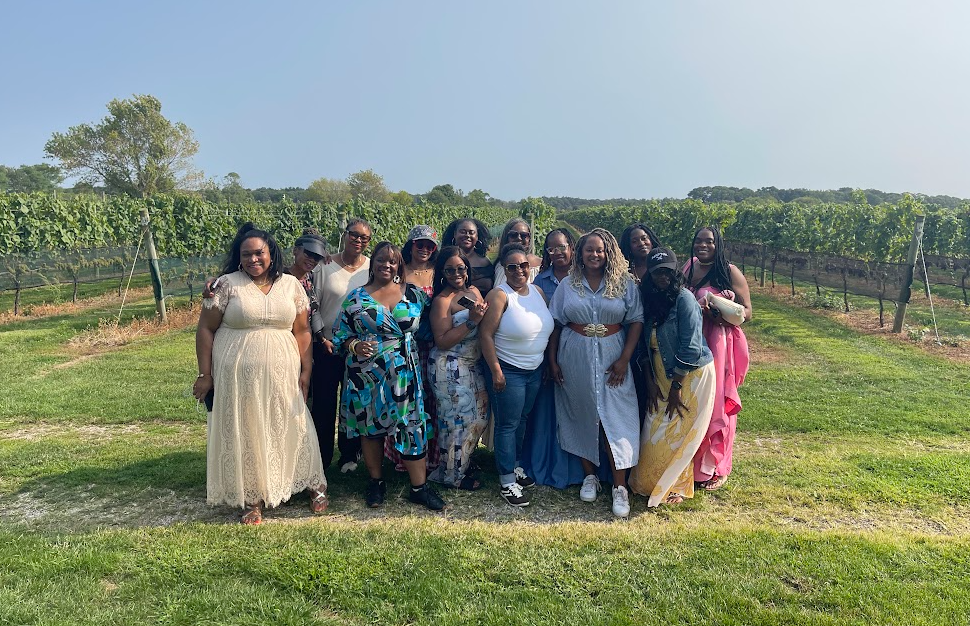Group of Black women posing together in a vineyard on a sunny day, dressed in stylish, colorful outfits, celebrating friendship and connection.