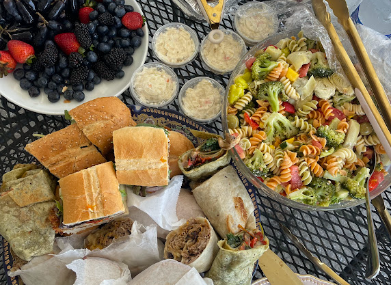 A spread of assorted food items including sandwiches, wraps, colorful pasta salad, and a variety of fresh berries on a table.