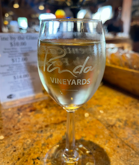 A glass of wine from Pindar Vineyards filled with a light-colored white wine, set against a rustic wooden background with an informal menu nearby.